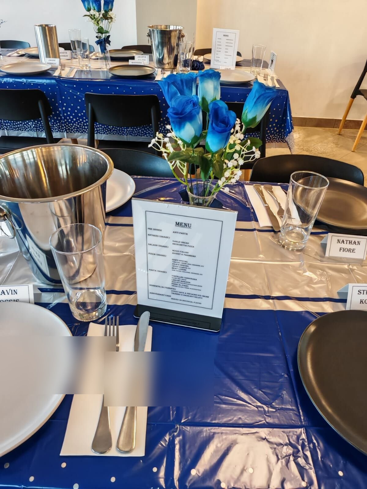 Long table set with blue tablecloths, plates and glassware by the window